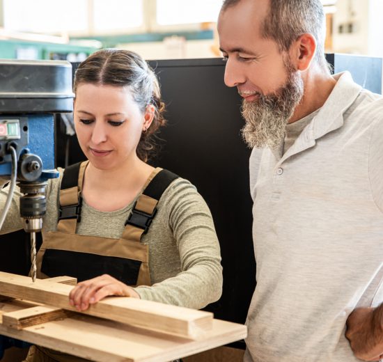 Auszubildende in der Lehre mit Matura bekommt in der Werkstatt etwas erklärt.