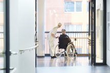 Eine Pflegekraft steht neben einer Frau im Rollstuhl in einem Krankenhaus. In Österreich herrscht ein Pflegenotstand.