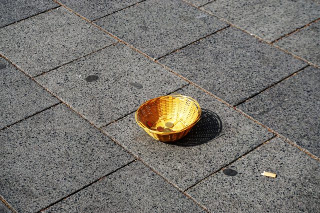 Flechtkorb eines Obdachlosen Bettler mit Kleingeld auf der Straße. Symbolbild Einmalzahlungen in der Inflation Almosen