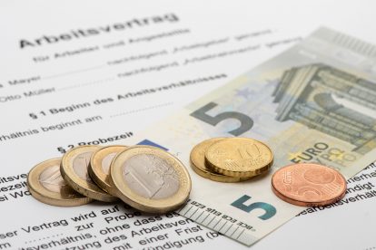 arbeitsvertrag mit Geld darauf. Euro. Münzen undScheine. Symbolbild: Mindestlohn in Österreich.