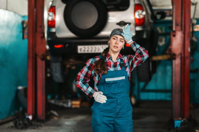 Eine Auszubildende zur Automechanikerin vor einer Auto. Sie wischt sich den Schweiß von der Stirn. Lehrlinge trifft die Inflation besonders stark.