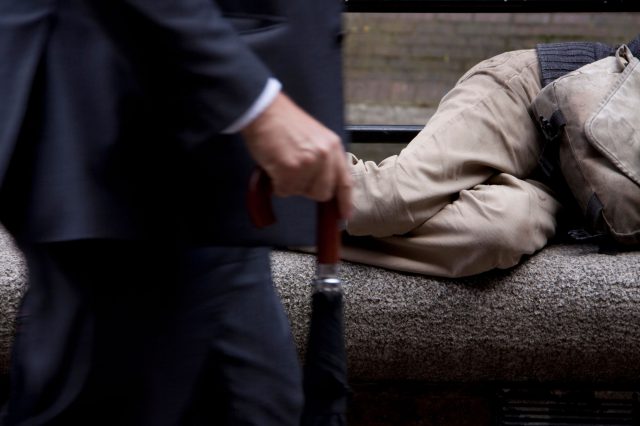 Ein reicher Geschäftsmann geht an einem Obdachlosen vorbei. Symbolbild fürVermögensungleichheit in Österreich.