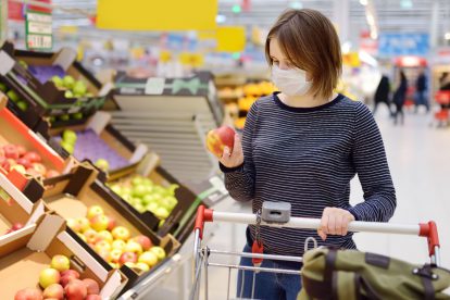 Ein Frau mit Maske betrachtet im Supermarkt einen Apfel. Symbolbild für die Debatte über die Inflation.