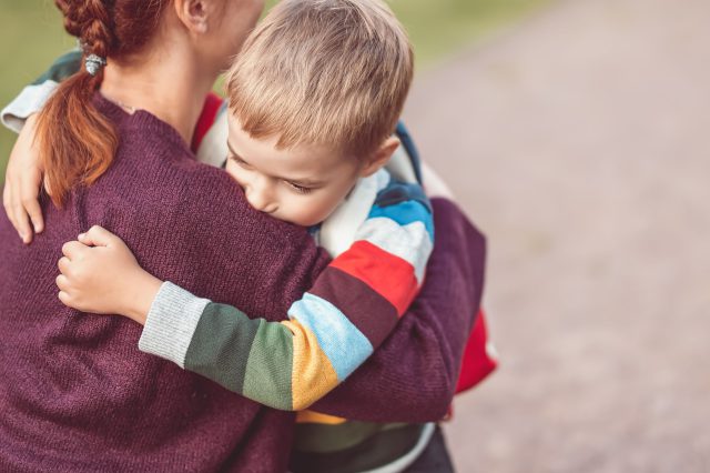 Ein kleiner Junge umarmt seine Mutter vor der Schule. Symbolbild für Österreichs Bildungssystem.