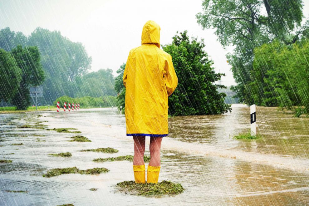 Eine Frau steht im Regenmantel und Gummistiefeln im Hochwasser. Sym,bolbild für Stagflation in Österreich.