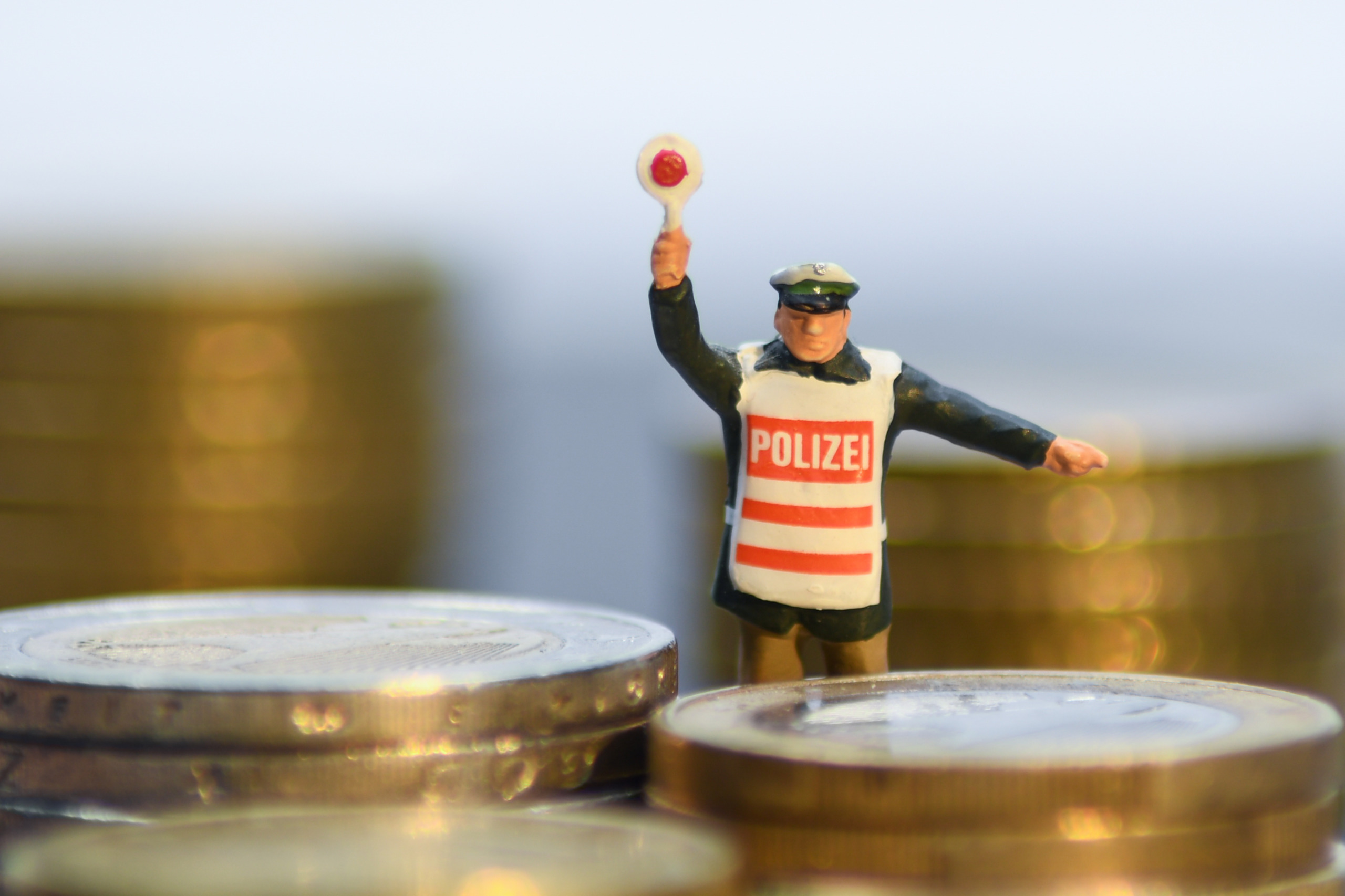 Ein Polizist als Figur will Geldmünzen umleiten. Symbolfoto für die Steuerlücke in Österreich, die durch Steuerbetrug entsteht.