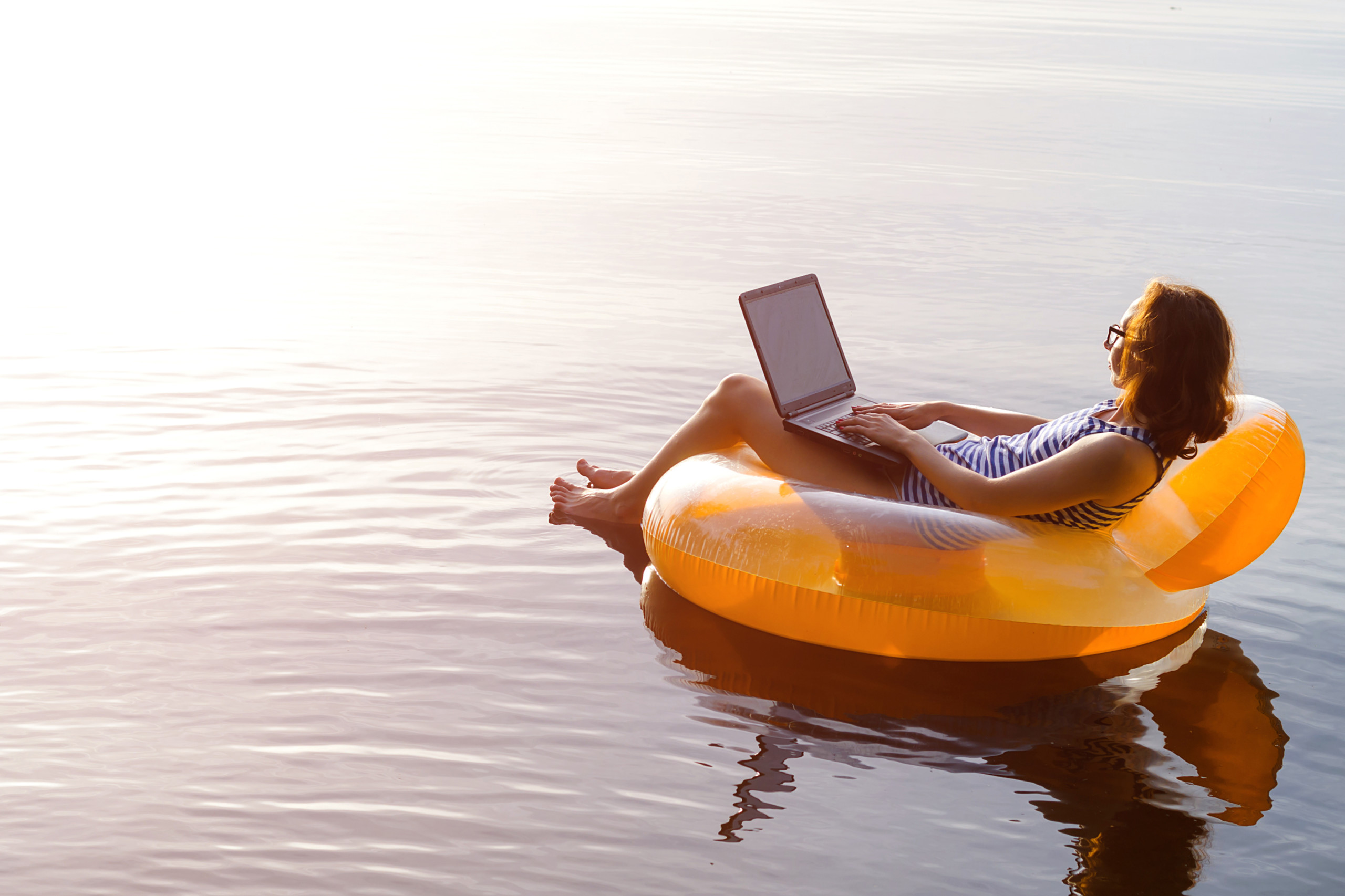 Eine Frau arbeitet auf einer Luftmatratze an ihrem Laptop. Symbolbild für die work-Life-Balance.