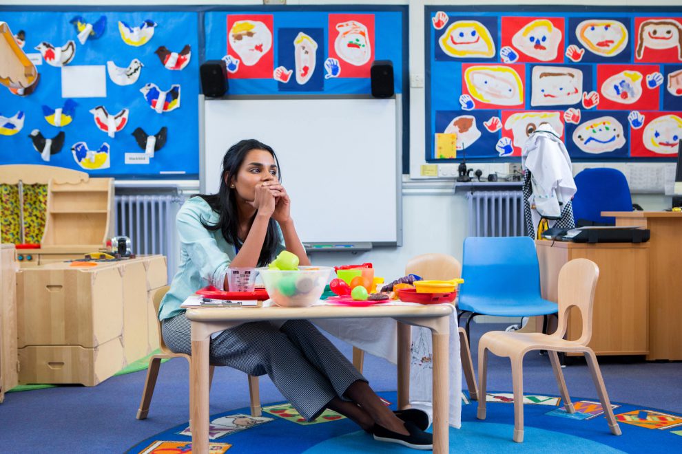 Eine Lehrerin sitzt frustriert an einem Tisch in der Schule. Symbolbild für den Lehrer:innenmangel. Lehrermangel.