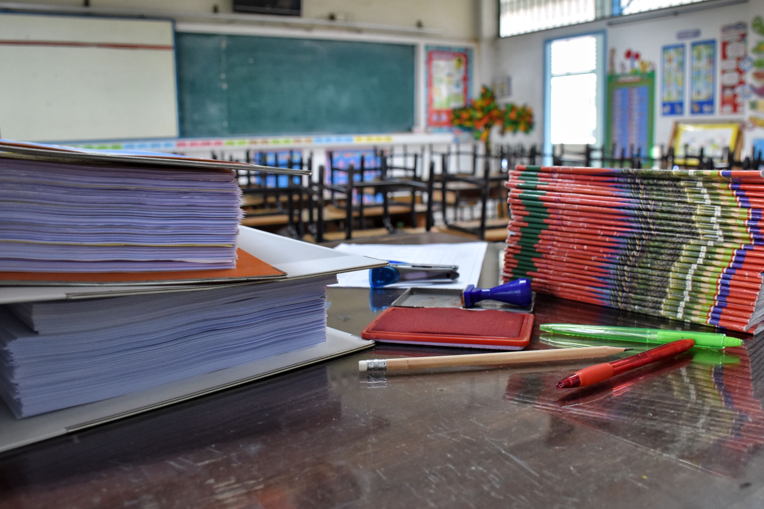 Eine leerer Klassenraum in einer Schule. Auf dem Pult stapeln sich die Aufgabenhefte. Symbolbild für den Lehrer:innenmangel. Lehrermange.