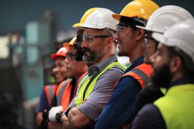 Arbeiter und Arbeiterin in einer Fabrik mit Helm. Symbolbild für die Ergebnisse der Herbstlohnrunde.