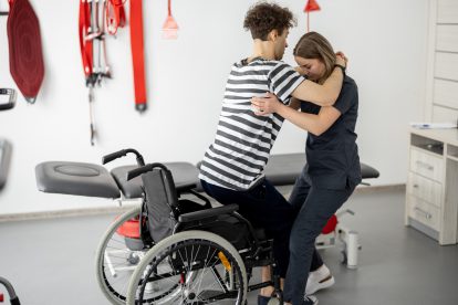 Eine Pflegerin hebt einen behinderten Mann aus dem Rollstuhl. Pflege ist Schwerarbeit.
