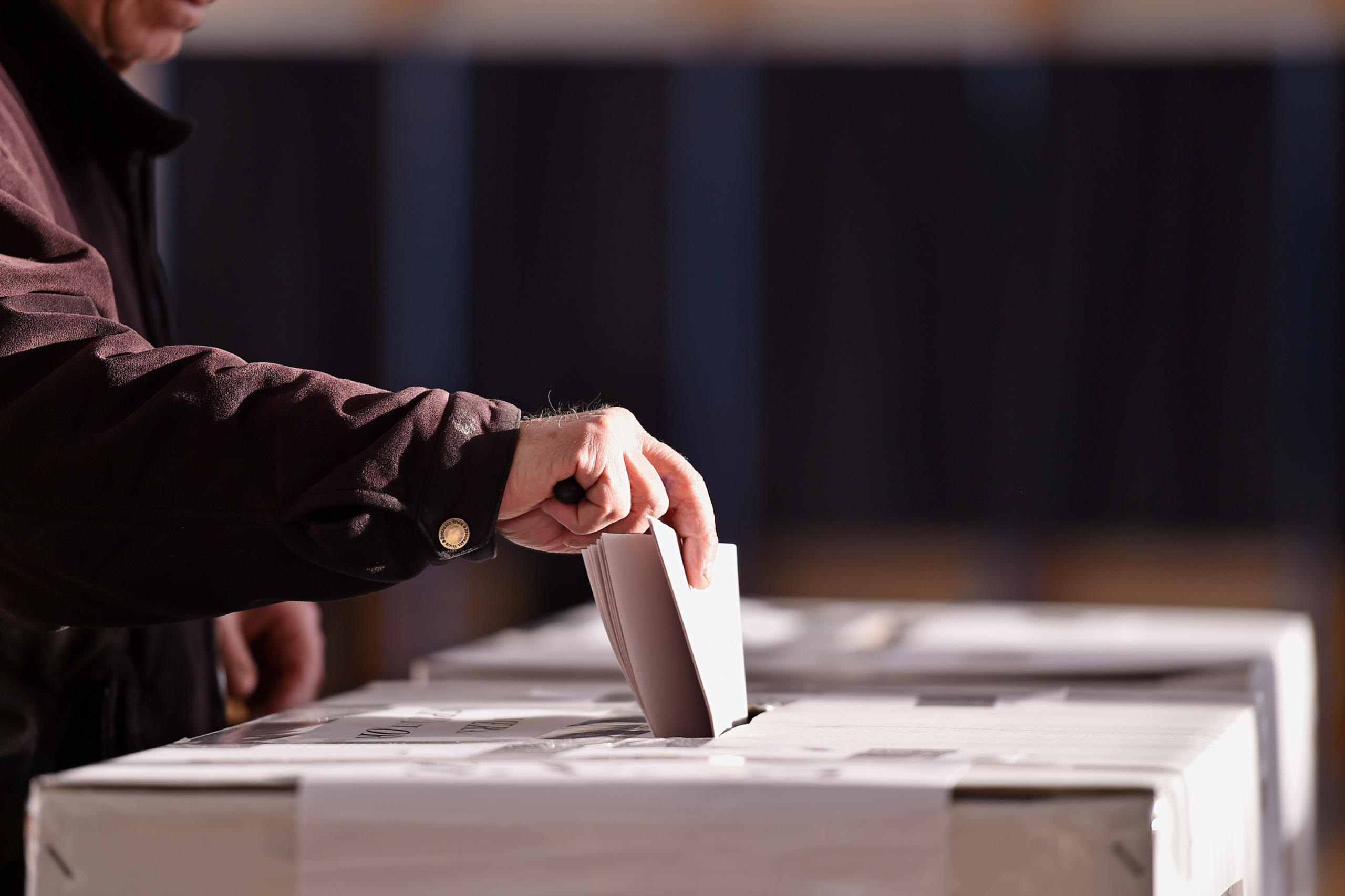 Ein älterer Mann steckt bei einer Wahl seinen Stimmzettel in eine Wahlurne. Symbolbild für die Demokratie in Österreich.