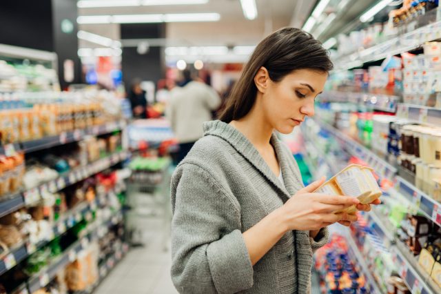 Eine Frau steht im Supermarkt und betrachtet die Preise. Symbolbild für die Konjunkturprognose 2023 für Österreich.