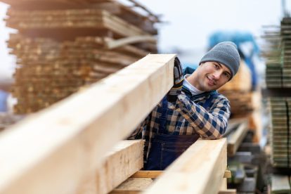 Ein Bauarbeiter hebt einen Holzbalken hoch. Symbolbild für die Mitbestimmung dank Nachhaltigkeitsbericht.