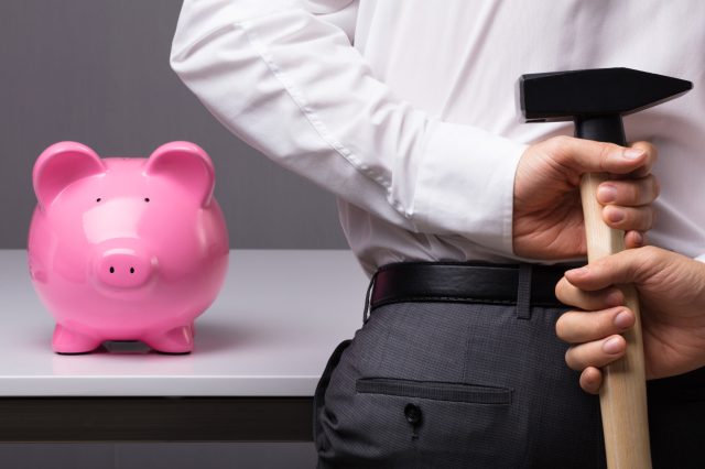 Ein Geschäftsmann mit Hammer will ein Sparschwein schlachten. Symbolbild Nationalbank Verlust.