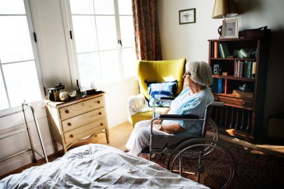 Eine ältere Frau im Rollstuhl sitzt alleine in ihrem Zimmer und wartet auf die 24-Stunden-Betreuung.