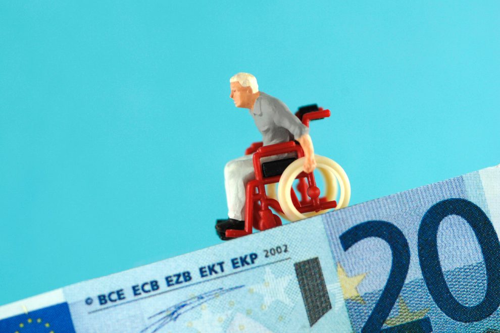 Eine Figürchen im Rollstuhl fährt einen zwanzig Euro schein hinab. Symbolbild Förderung 24-Stunden-Betreuung.