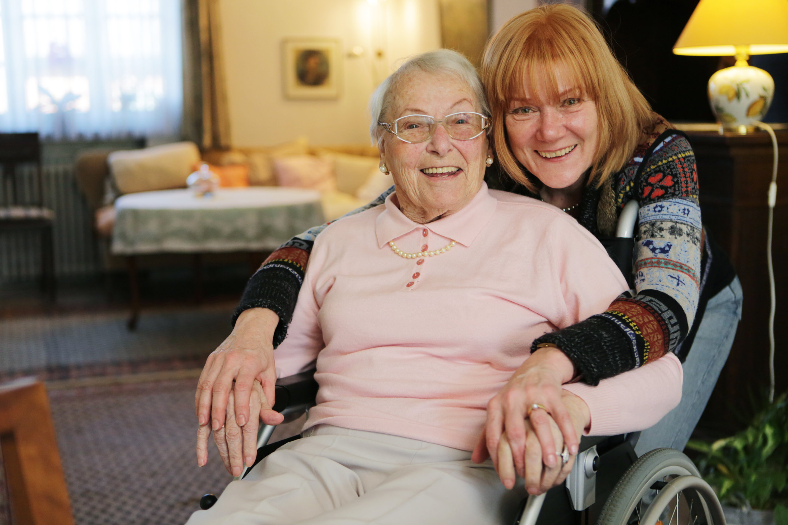 Eine ältere Frau im Rollstuhl lächelt gemeinsam mit der 24-Stunden-BEtreuung.