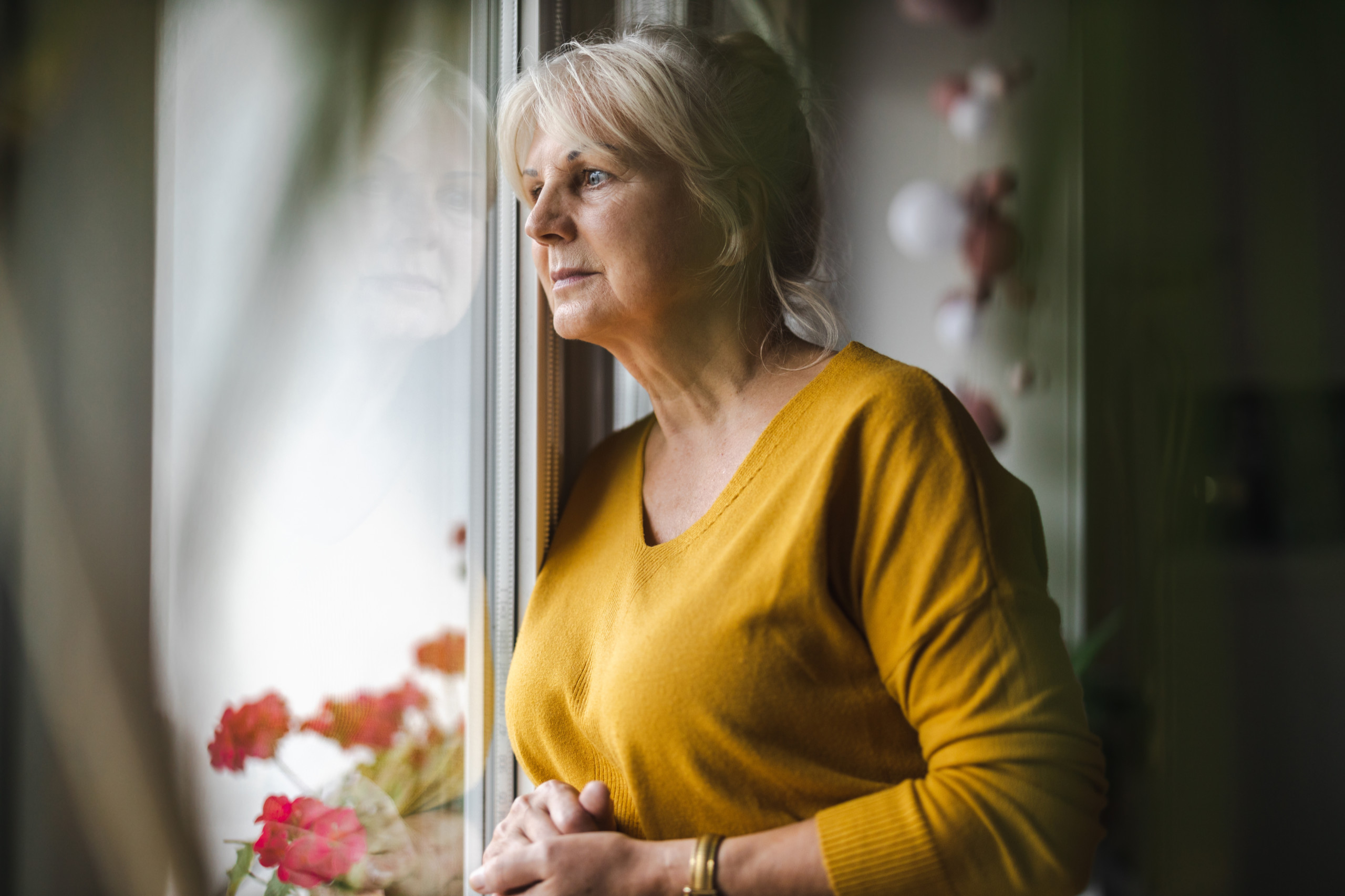 Eine Pensionistin steht am Fenster und schaut nach draußen. Symboldbild für die Pensionskassen.