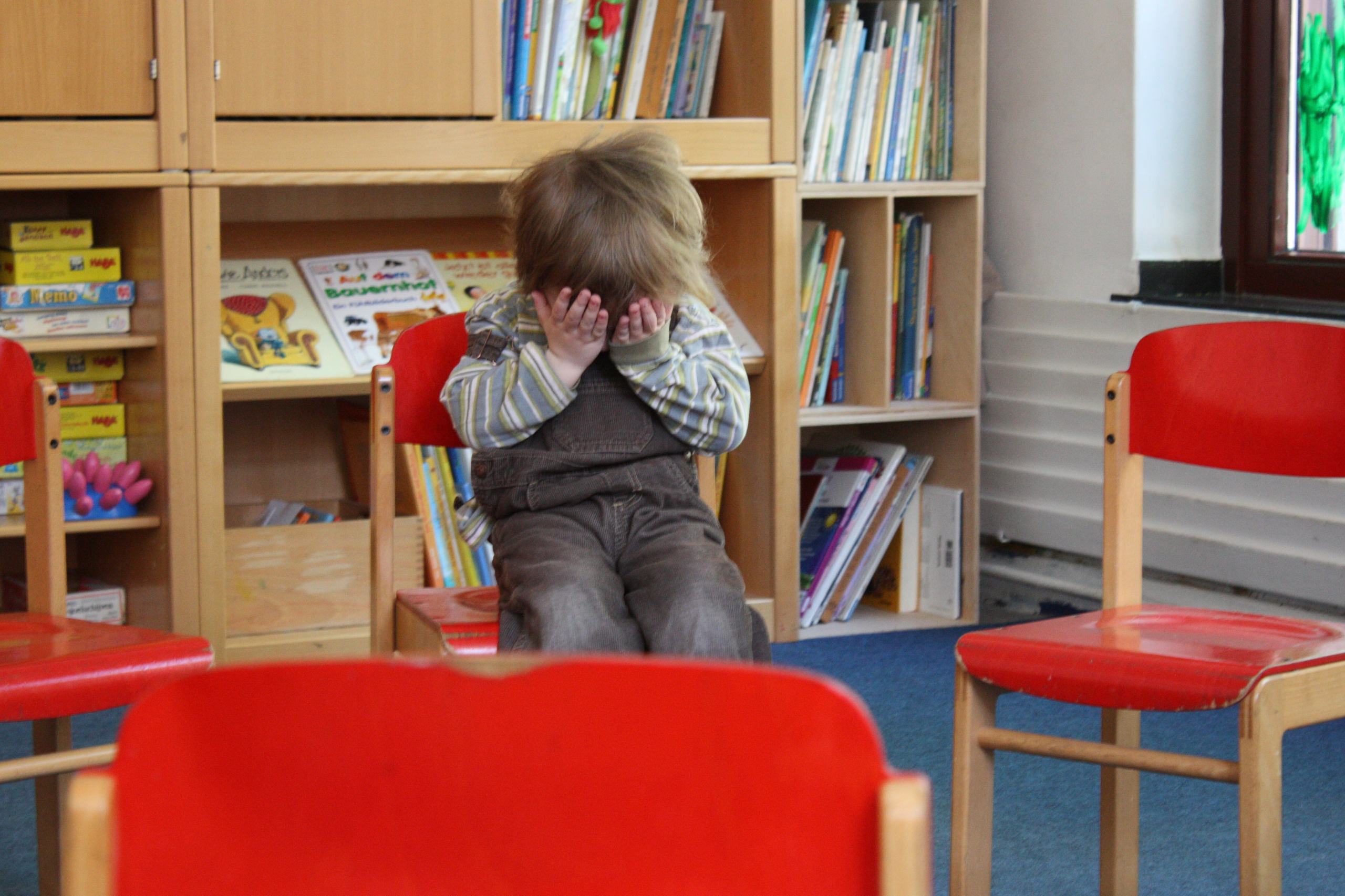 Ein kleiner Junge im Kindergarten hält sich die Hände vor das Gesicht. Symbolbild für den Tag der Elementarpädagogik.