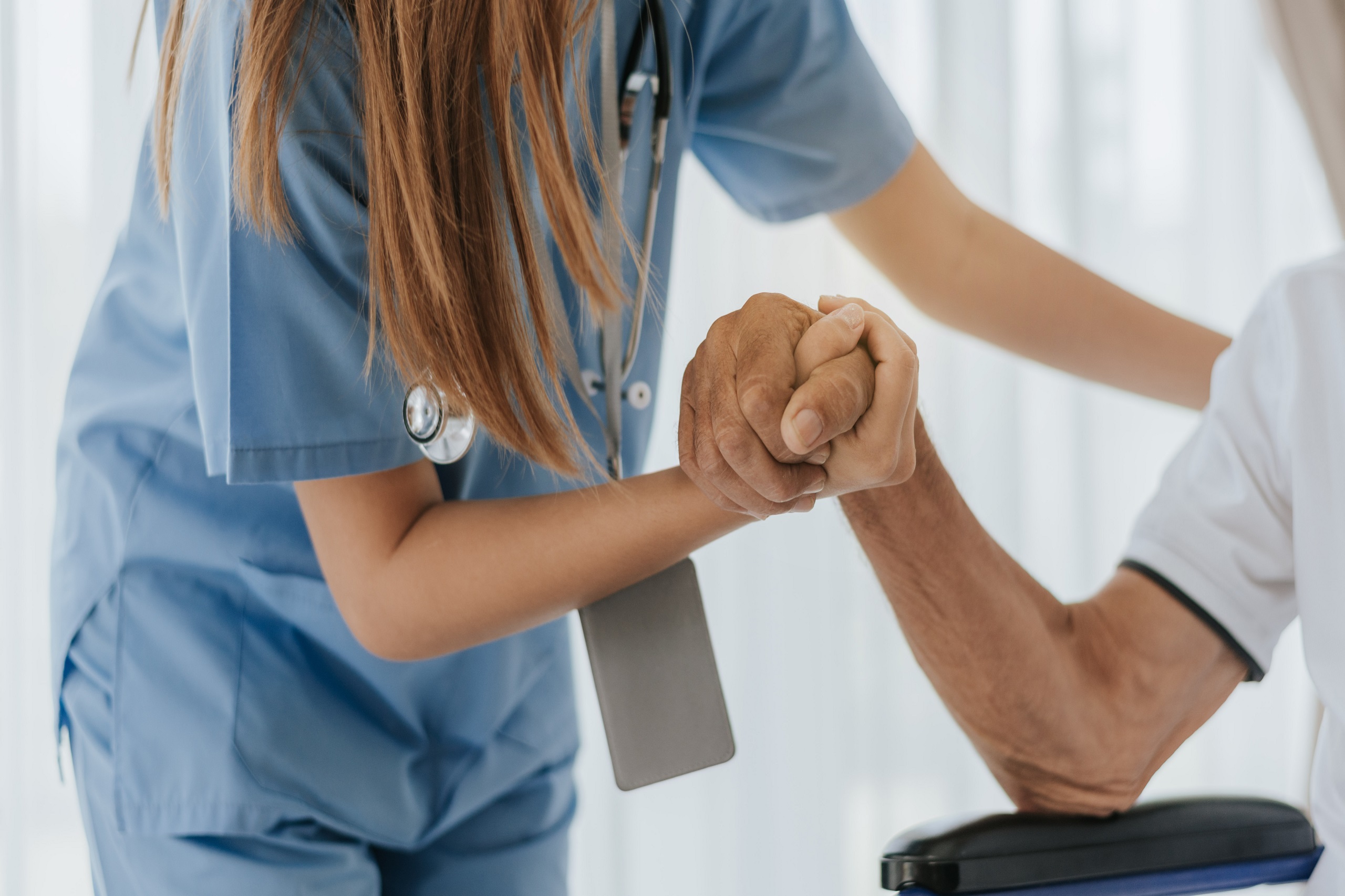Eine Frau in Pflegeuniform hält die Hand eines älteren Herrn. Symbolbild für die KV-Verhandlungen in Privatkrankenanstalten.