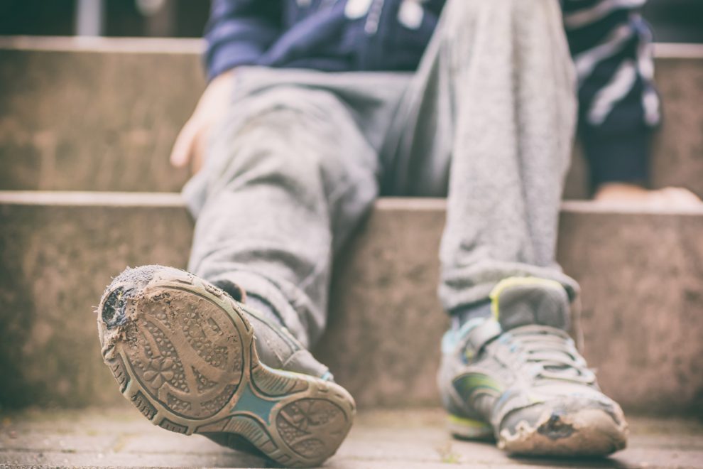 Ein armes Kind zeigt seine kaputten Schuhe. Symbolbild für Kinderarmut.