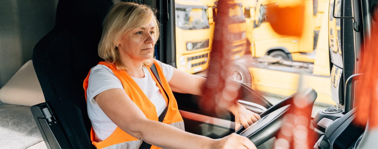 Eine Frau trägt eine Sicherheitsweste und sitzt am Steuer eines LKWs. Symbolbild für die schlechten Arbeitsbedingungen von Berufslenker:innen.