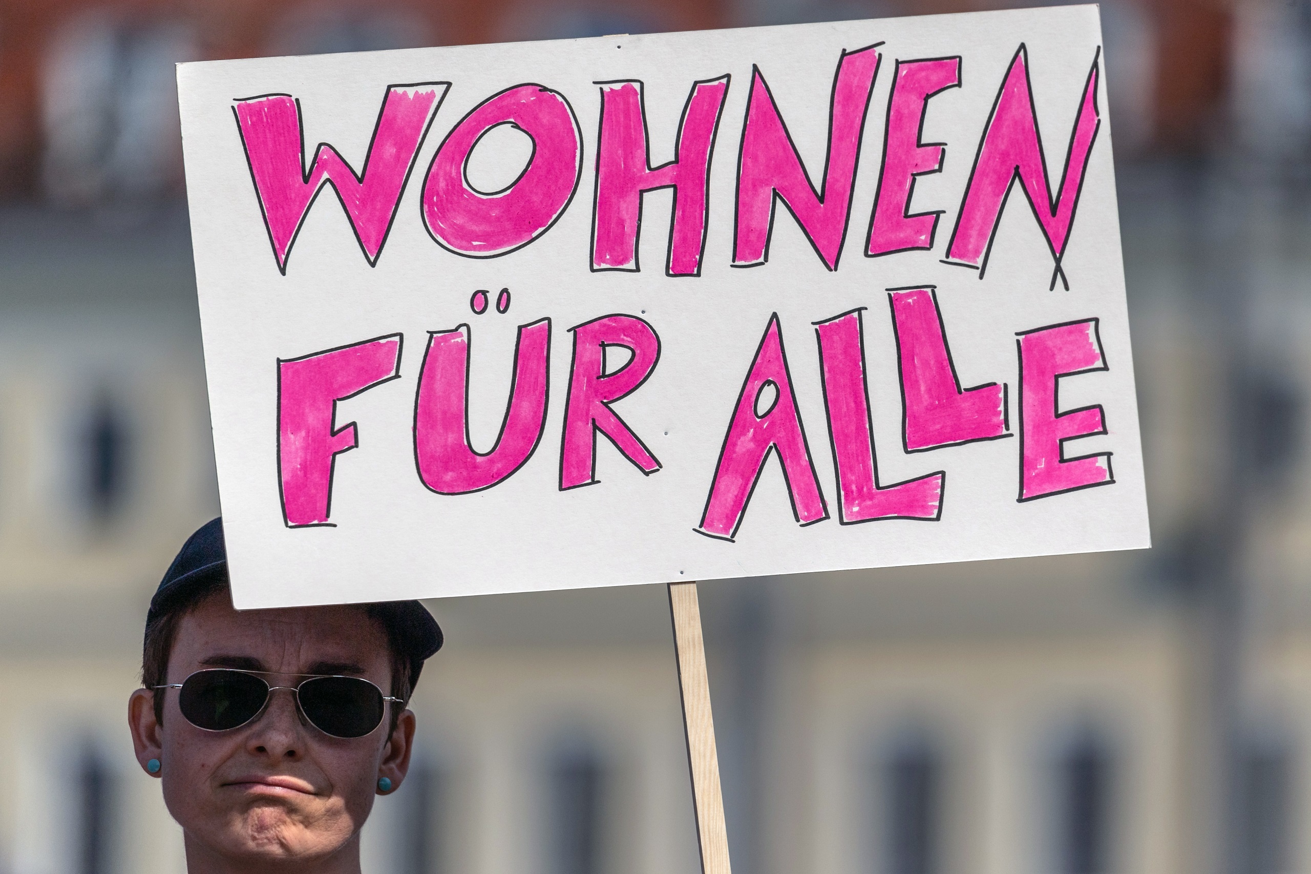 Eine Frau demonstriert mit dem Schild "Wohnen für alle". Symbolbild für das Grundrecht Wohnen.