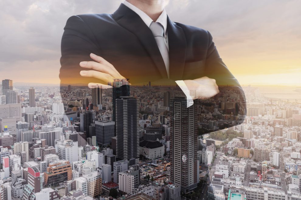 Ein Mann im Anzug steht halb durchlässig vor dem Panorama einer Stadt. Symbolbild für Immobilieninvestor:innen.