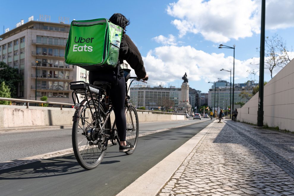 Eine:r Plattformarbeiter:in sitzt auf einem Fahrrad mit einer Tasche mit der Aufschrift Uber Eats.