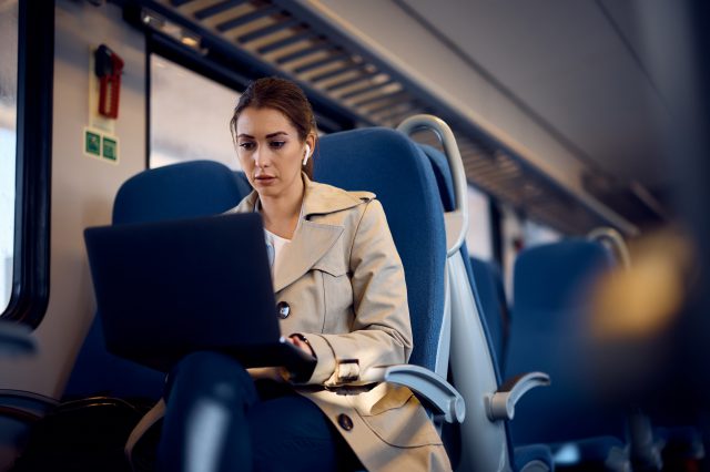 Frau sitzt in einem Zug und arbeitet an ihrem Laptop. Symbolbild für klimafittes Pendeln.