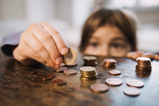 Ein Kind steht an einem Tisch und zählt Geld. Symbolbild für die mangelhafte Sozialhilfe.