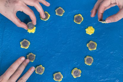 Bild von einem blauen Kuchen mit gelben Sternen, der die EU-Flagge darstellen soll. Hände legen 1-Euro-Münzen auf die Sterne. Symbolbild für die Fiskalregeln.