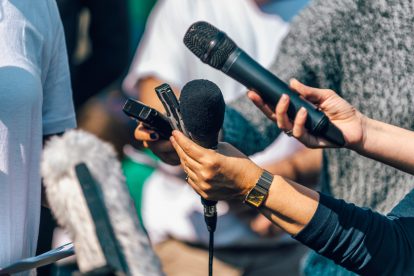 Menschen mit Mikrofonen und Diktiergeräten in der Hand interviewen eine Person. Symbolbild für die schwierigen Arbeitsbedingungen von Journalist:innen.