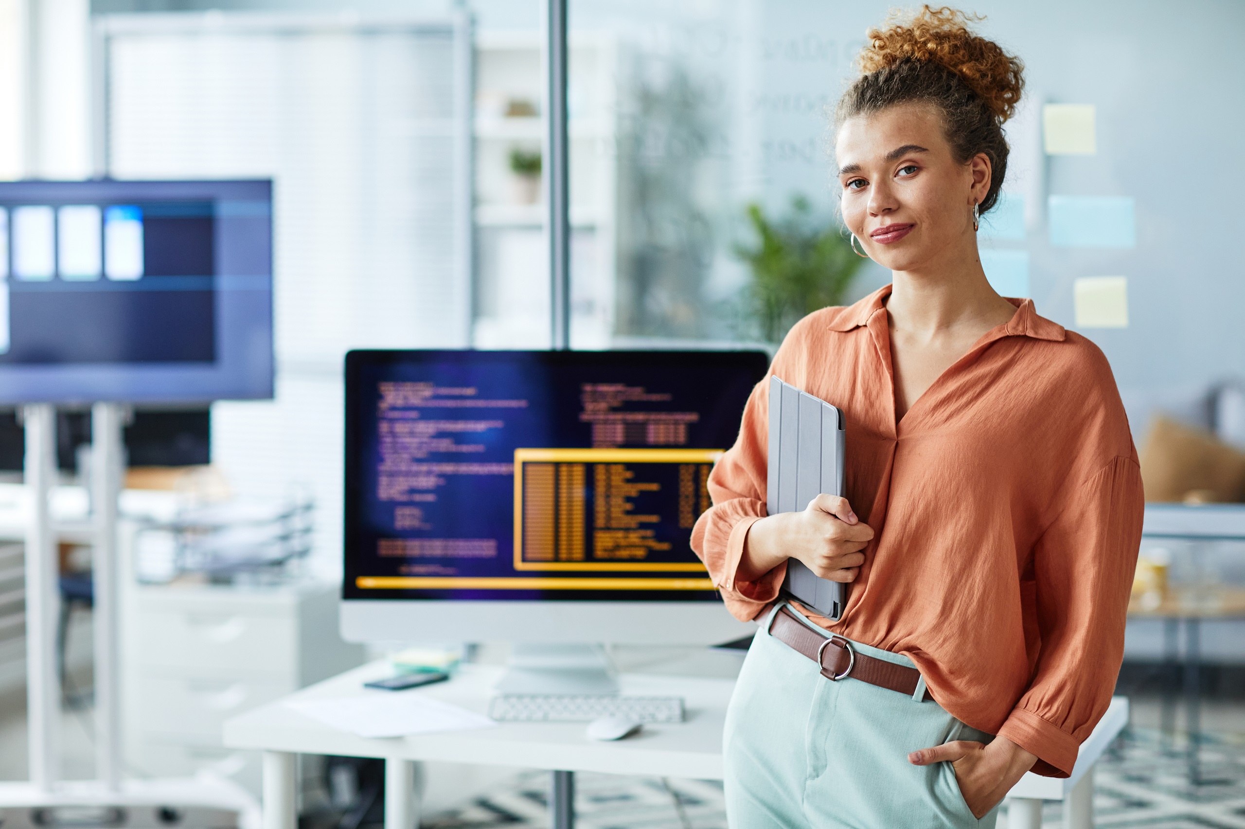 Eine Frau steht vor einem Computer mit Codes und hält ein Notizbuch. Symbolbild für mehr Frauen in technischen Lehrberufen.