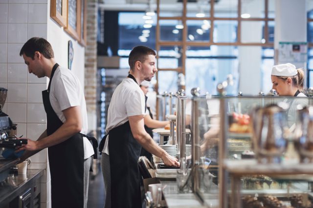 Kellner und Kellnerin und Köche und Köchin in einem Restaurant. Symbolbild für den Arbeitsklima Index.