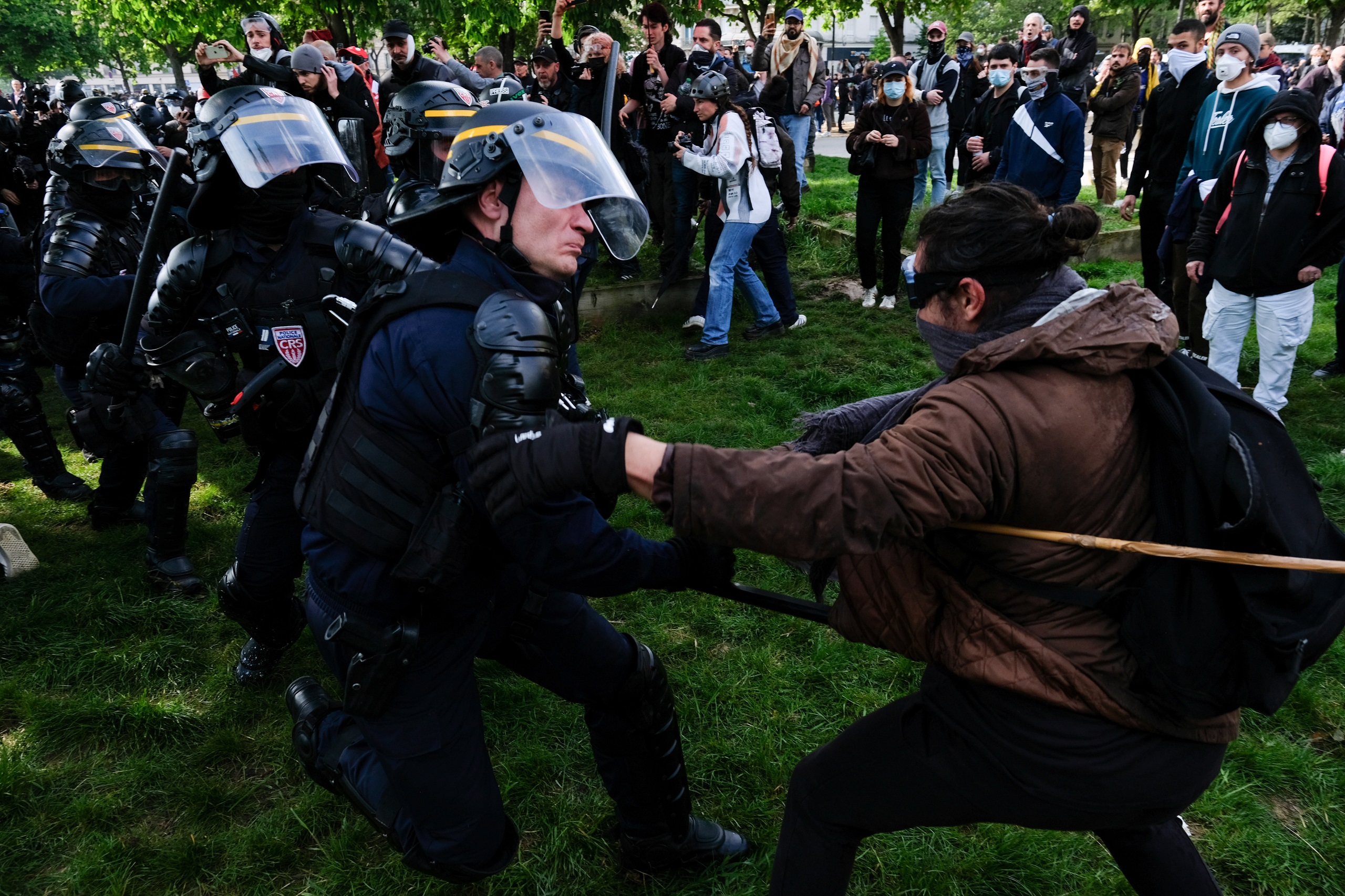 Ein Polizist geht mit Schlagstock auf einen Demonstranten los. Im Hintergrund sind andere Demonstrierende zu sehen. Symbolbild, dass die Polizeigewalt auf Demonstrationen gegen die Rentenreform Macrons zeigen soll.