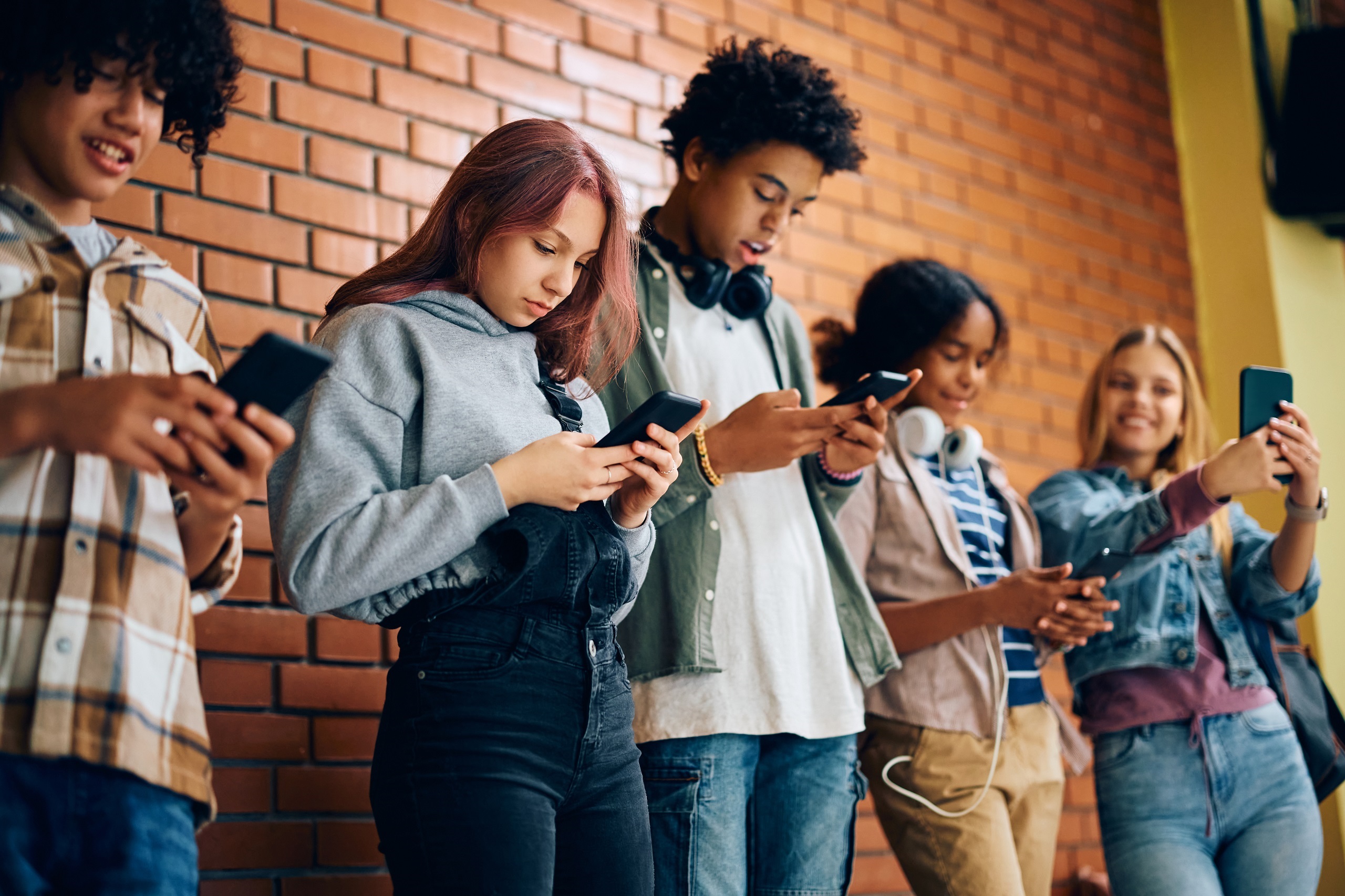 Jugendliche stehen an einer Wand und schauen auf ihr Handy. Symbolbild für Digitalisierung und Schule.