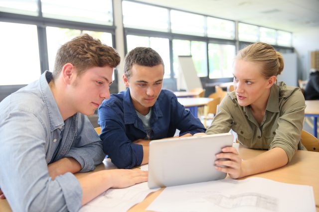 Zwei Schüler und eine Schülerin arbeiten an einem Tablet. Die Schülerin zeigt etwas am Tablet. Symbolbild für Digitalisierung und Schule.