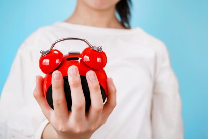 Eine Frau hält einen roten Wecker in der Hand. Ein Symbolbild für individuelle arbeitszeit.