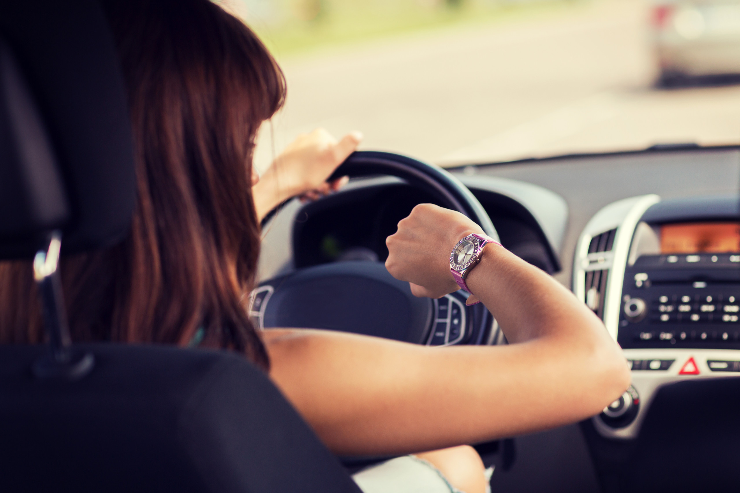 Eine Frau sitzt in ihrem Auto und schaut auf ihre Armbanduhr. Sie arbeitet nicht im Homeoffice.