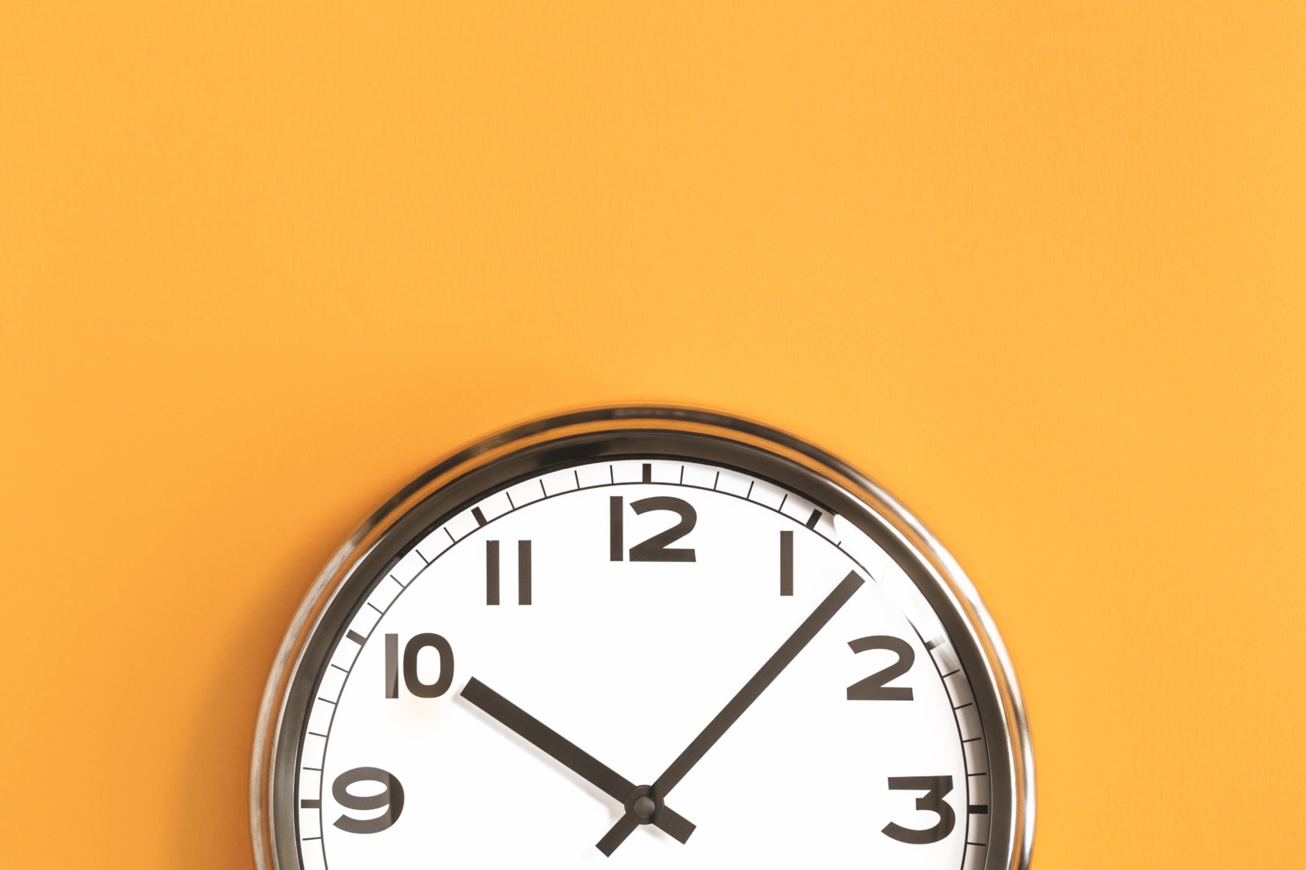Eine Uhr vor einer gelben Wand. Symbolbild für die Arbeitszeitverkürzung in Österreich auf eine 32-Stunden-Woche bei vollem Lohnausgleich.
