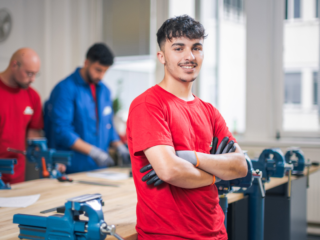 Hazem Almater steht lächeln an einer Werkbank. Dank Öko-Booster macht er eine Ausbildung. 