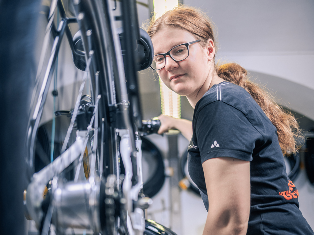 Sarah Sutlovic steht vor einem Fahrrad und repariert es. Symbolbild für den Lehrberuf Fahrradmechatroniker:in