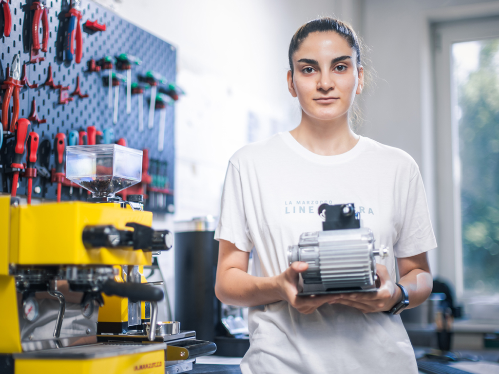 Sarah Zand hält ein repariertes Teil einer Espressomaschine in die Kamera. Sie nlernt über Öko-Booster und die Umweltstiftung einen Beruf.