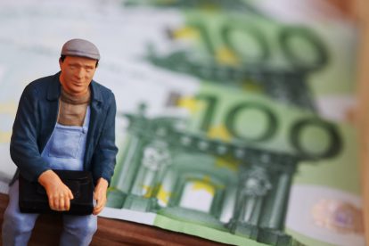 Eine kleine Figur mit Kind in einem Tragegurt steht vor einem 100-Euro-Schein. Symbolbild für Arbeitslosengeld.