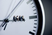 Figürchen sitzen auf dem Stundenzeiger einer analogen Uhr. Symbolbild für die Arbeitszeit in Österreich.