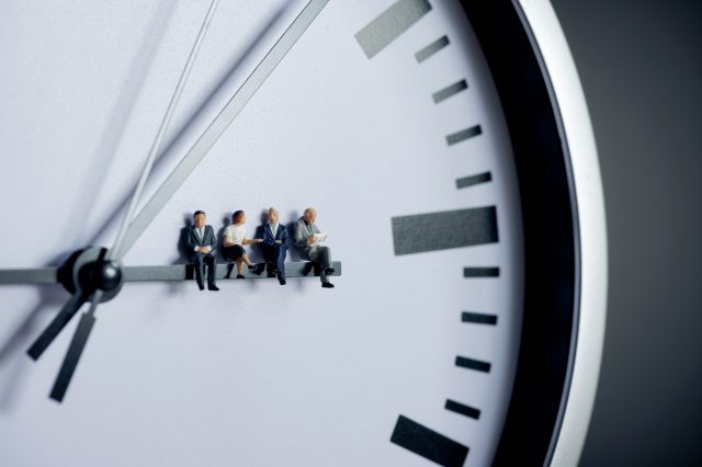 Figürchen sitzen auf dem Stundenzeiger einer analogen Uhr. Symbolbild für die Arbeitszeit in Österreich.