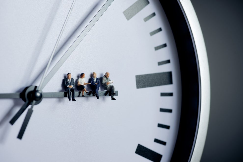 Figürchen sitzen auf dem Stundenzeiger einer analogen Uhr. Symbolbild für die Arbeitszeit in Österreich.