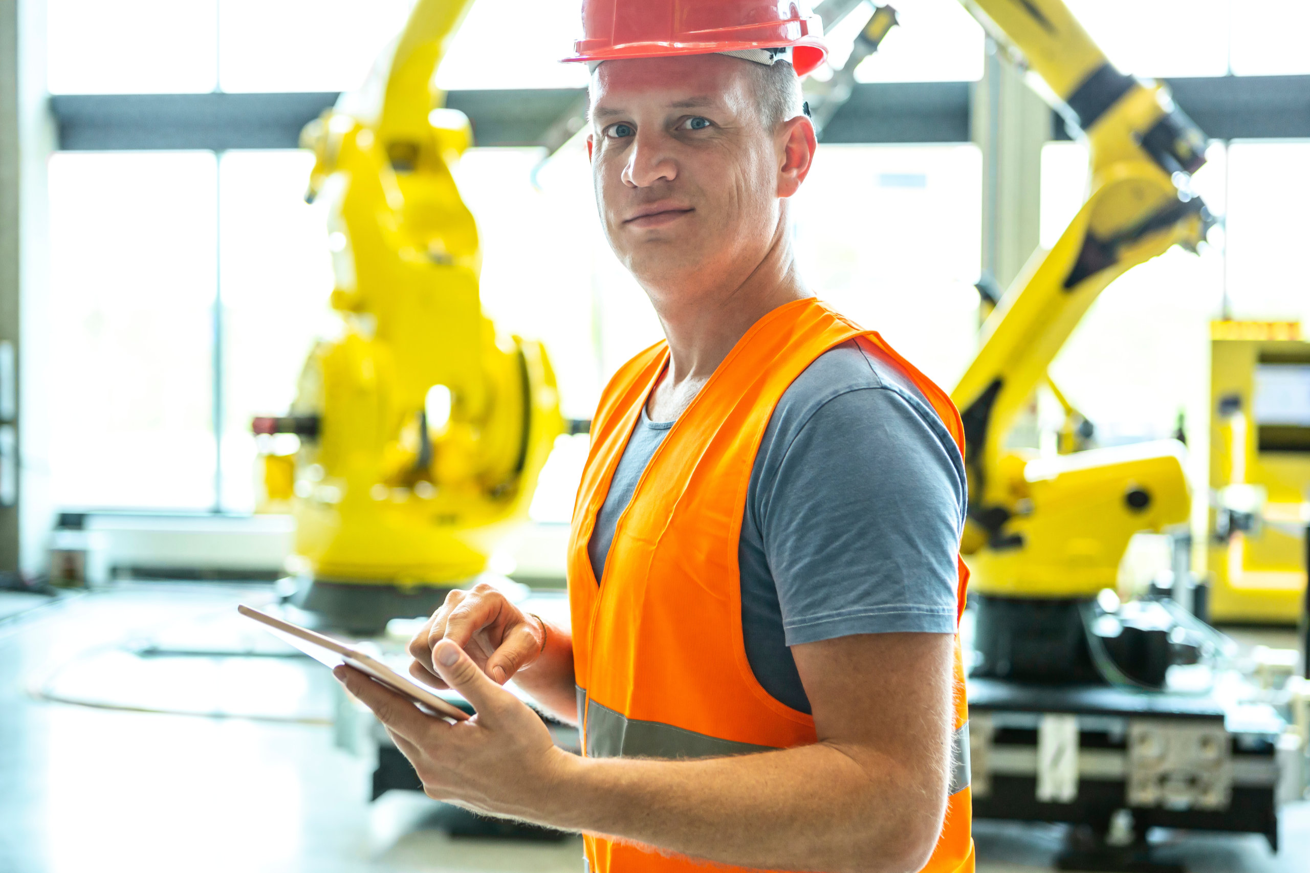Ein Arbeiter mit Helm und Weste hält in einer Fabrik ein Tablet in der Hand. Digitalisierung in Österreich.